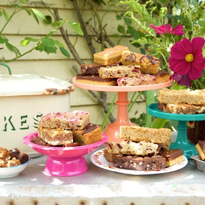 honeybuns gluten free cakes served on colourful tiered cake trays next to a cake tin on an outside garden table 
