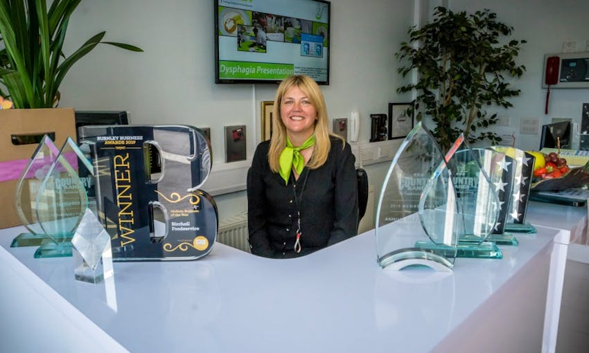 birchalls staff member sits behind the birchalls front desk surrounded by business awards and trophies 