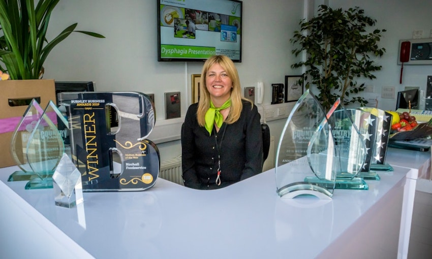 Recent winners of 'Medium Business of the Year' at the 2019 Burnley Business Awards birchalls staff member sits behind the birchalls front desk surrounded by business awards and trophies