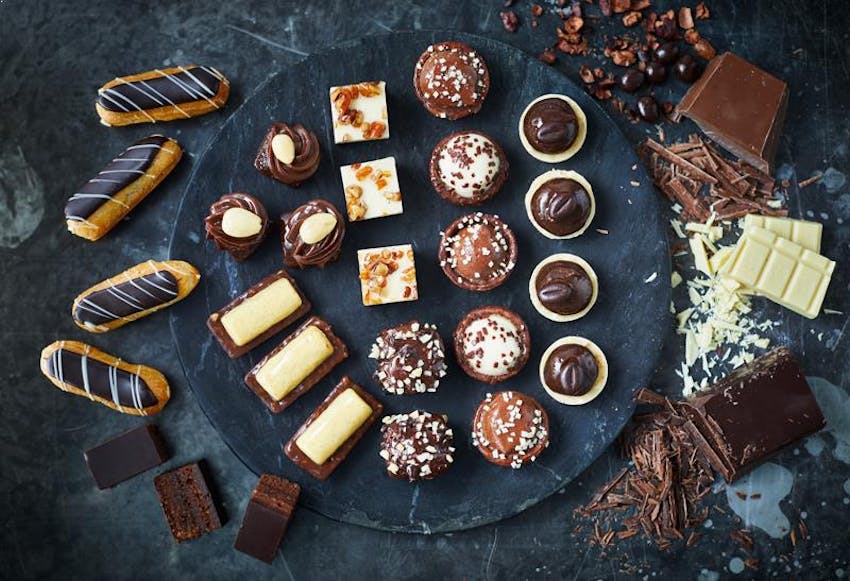 flatlay of brioche pasquier baked chocolate eclairs, brownie bits and chocolate treats on a dark marble surface 