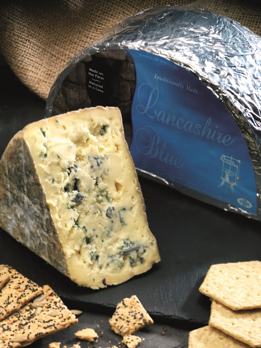 carron lodge lancashire blue cheese wheel with triangle slice on a black slate with various crackers 