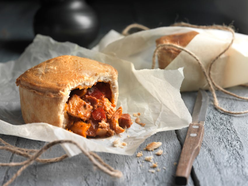 celtic pie co chicken and chorizo pie halved with filling pouring out onto baking paper on top of a grey wooden table