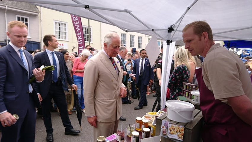 prince charles browsing the products on the otter vale farmers market stall with a crowd watching 