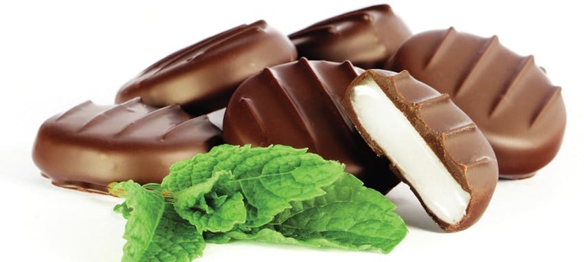 whitakers mint chocolate circles stacked on top of one another next to fresh mint leaves