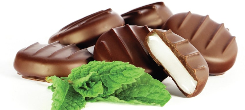 whitakers mint chocolate circles stacked on top of one another next to fresh mint leaves