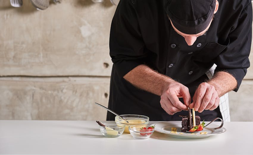 chef in black uniform carefully and cautiously decorates a dessert 