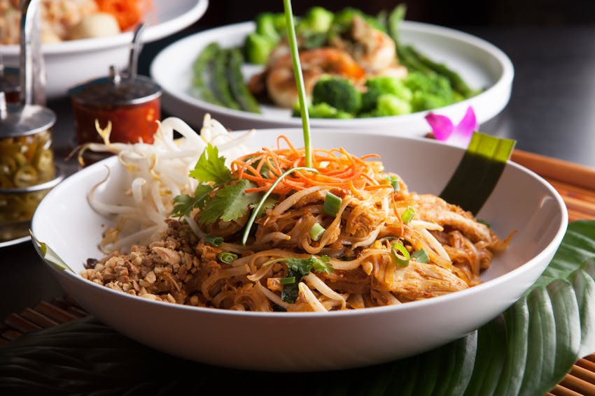 pad thai consisting of rice noodles, chicken, peanuts, eggs, bean sprouts and vegetables in a white dish 