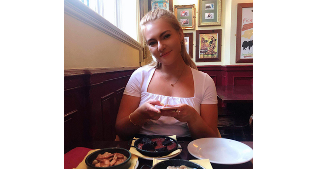 a young girl smiling at a restaurant dinner table behind three plates of tapas 