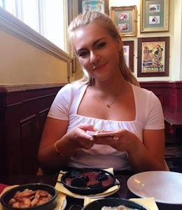 a young girl smiling at a restaurant dinner table behind three plates of tapas 