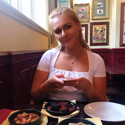 a young girl smiling at a restaurant dinner table behind three plates of tapas 