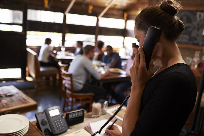 woman takes restaurant orders over the phone and writes them down on the front desk 