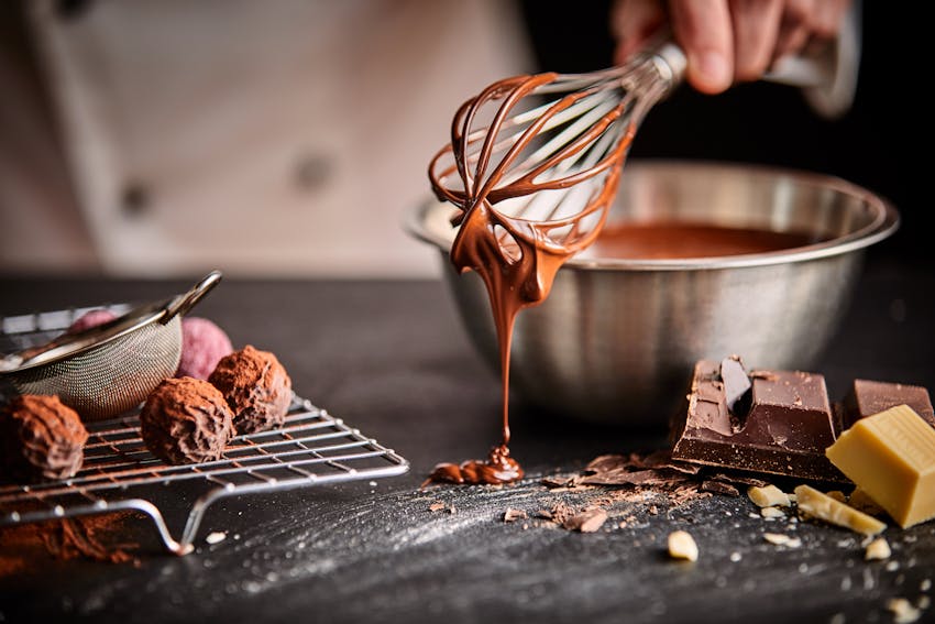 woman holding a whisk that has dairy free chocolate icing dripping onto the cooking work top  