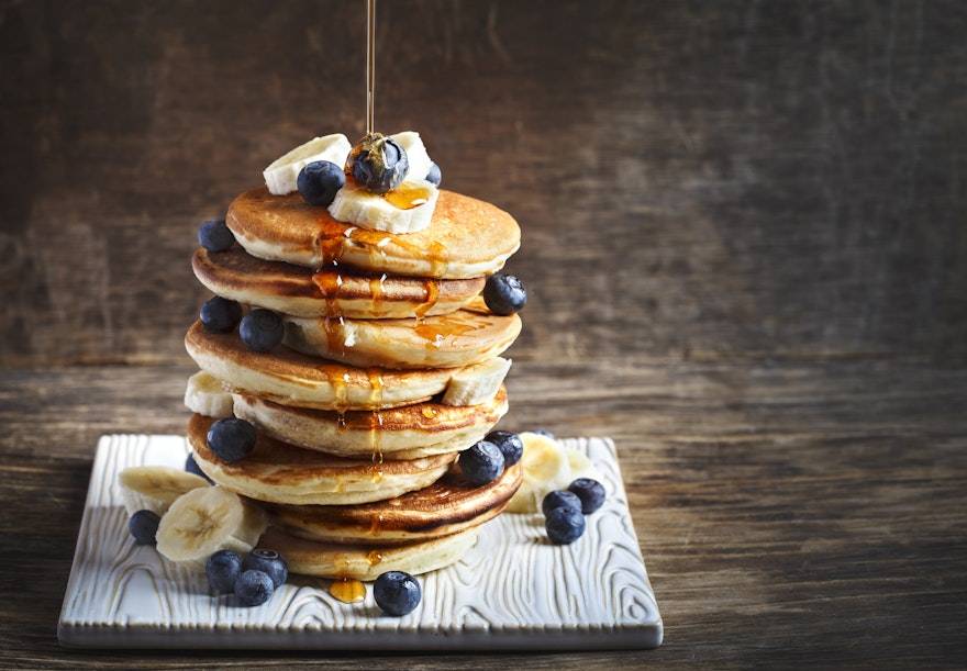 stack of fluffy american pancakes topped with banana blueberries and honey drizzle 