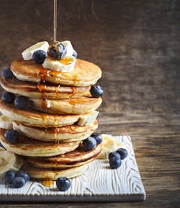 stack of fluffy american pancakes topped with banana blueberries and honey drizzle 