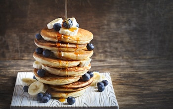 stack of fluffy american pancakes topped with banana blueberries and honey drizzle 