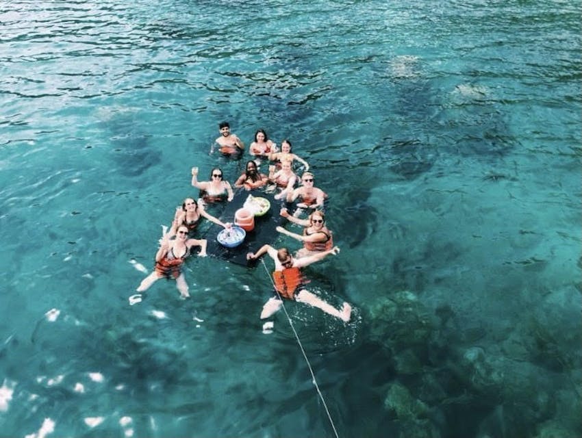 group of young adults having drinks on a floating table in the ocean 