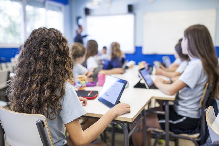 children sat at desks in a classroom listening to the teacher 