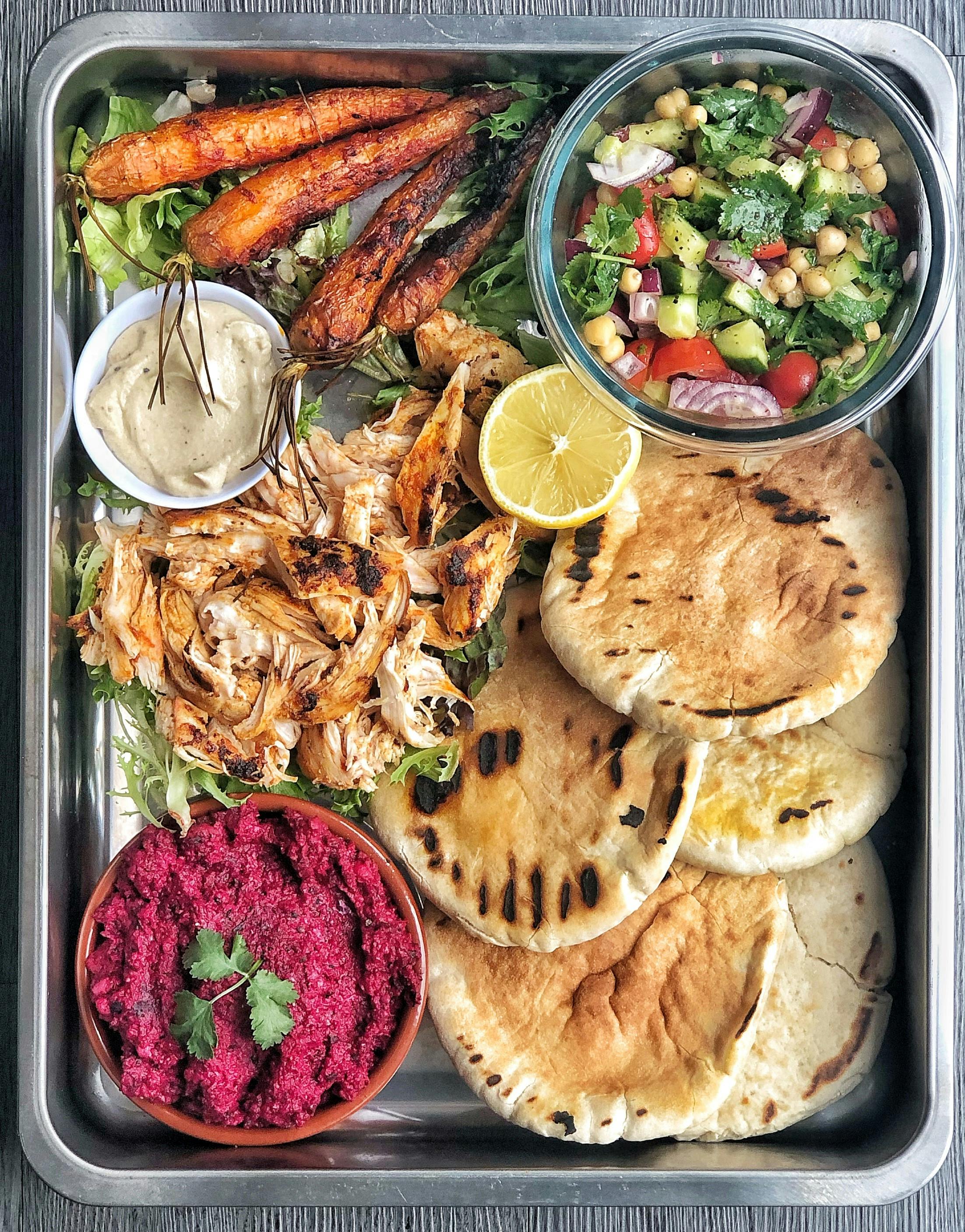baking tray of harissa chicken pittas with baked carrots vegetables shredded chicken and beetroot dip 