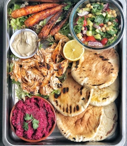 baking tray of harissa chicken pittas with baked carrots vegetables shredded chicken and beetroot dip 