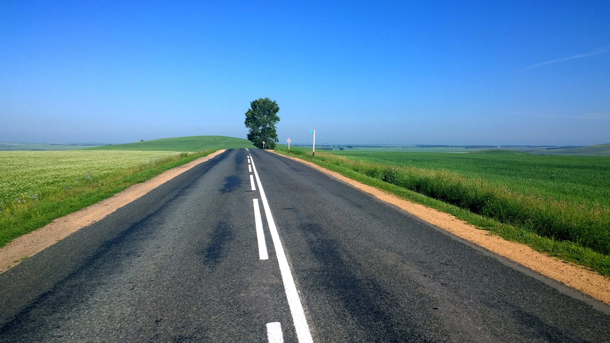 An empty straight road with green fields each side