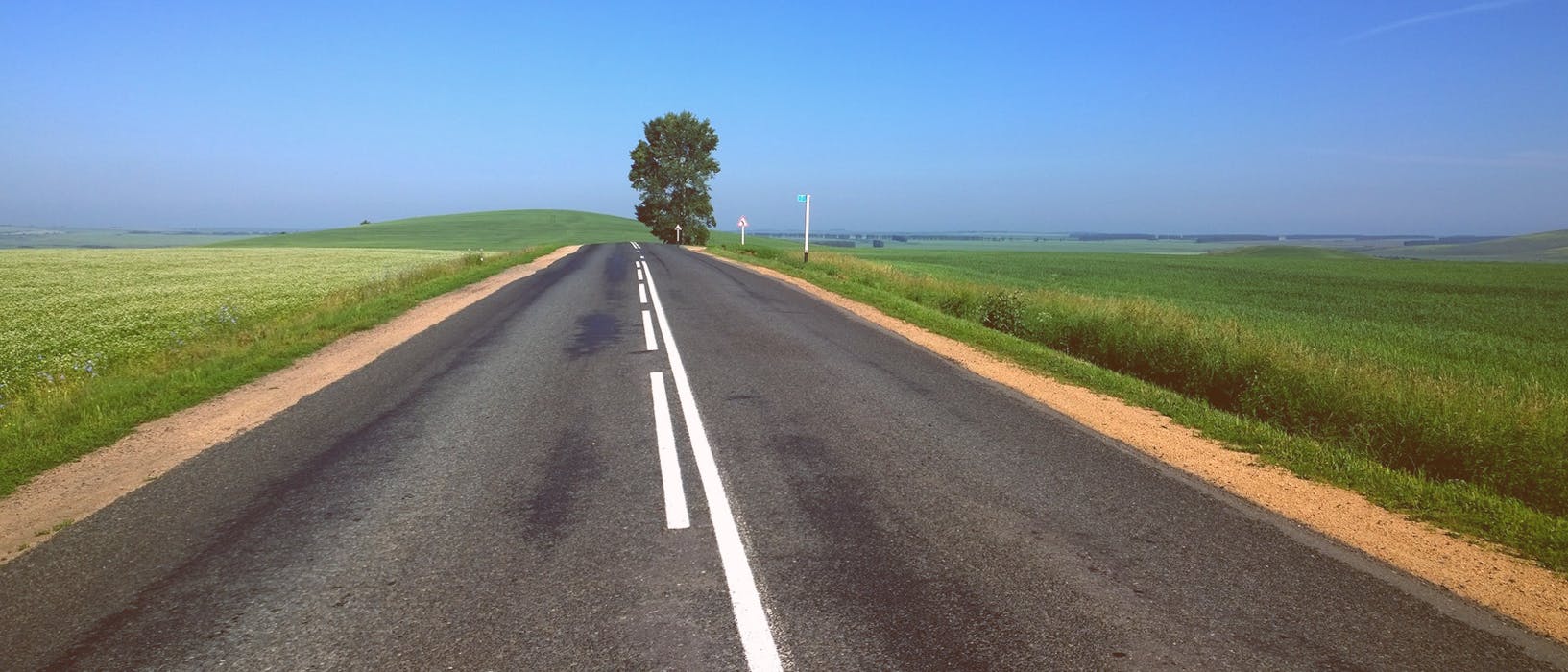 An empty straight road with green fields each side