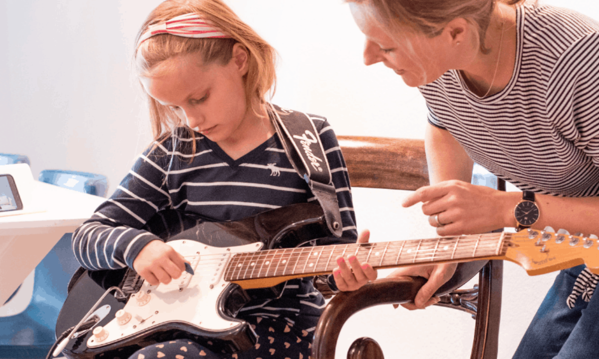 A woman teaching a child to play guitar