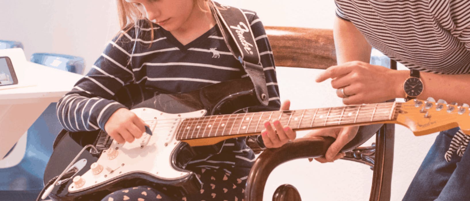 A woman teaching a child to play guitar