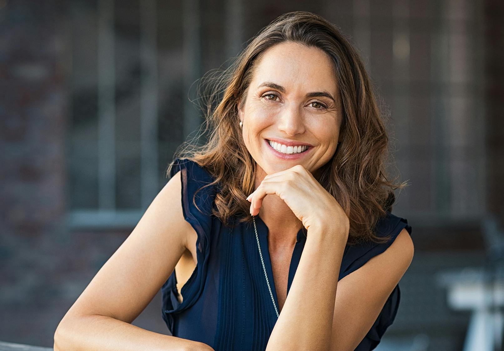 smiling woman in blue dress sitting at table with her hand on her chin