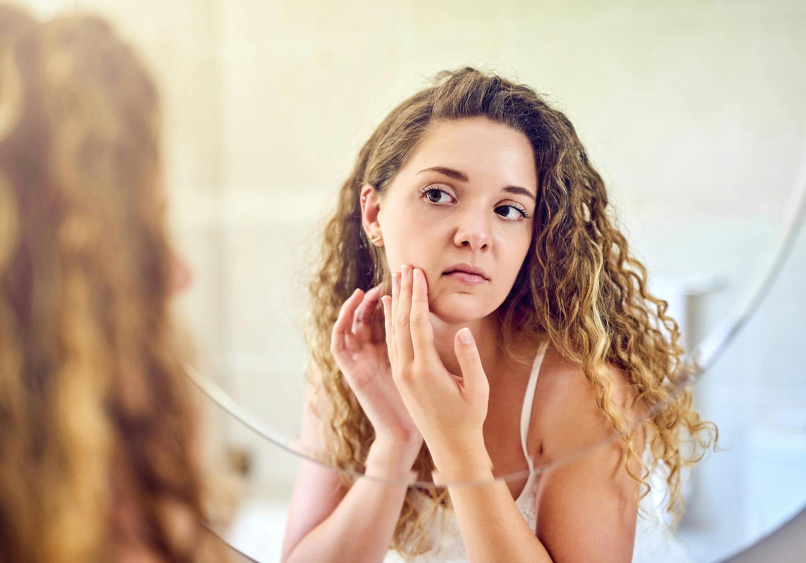Young woman inspecting the skin on her face in a mirror.