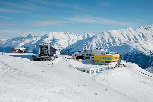 Winterbetrieb auf Corviglia mit Talstation Piz Nair Verschneite Skigebietsszene auf Corviglia oberhalb von St. Moritz im Engadin. Mehrere Skifahrer sind auf den Skipisten unterwegs. Im Hintergrund sind die Bergstation Corviglia und die Talstation Piz Nair in einer winterlichen Berglandschaft zu sehen.