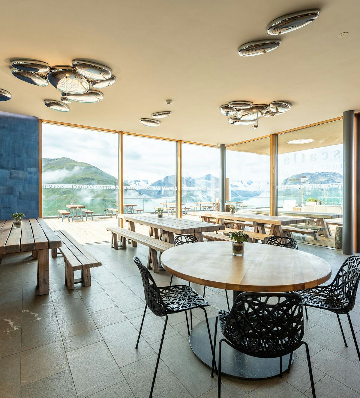 Scatla – pront’ a manger | Romantik Hotel Muottas Muragl | Sommer Das Restaurant Scatla – pront’ a manger auf Muottas Muragl präsentiert sich mit einem modernen, hellen Innenraum, Holztischen und einer grossen bodentiefen Fensterfront, die den Blick auf die Engadiner Bergwelt freigibt.