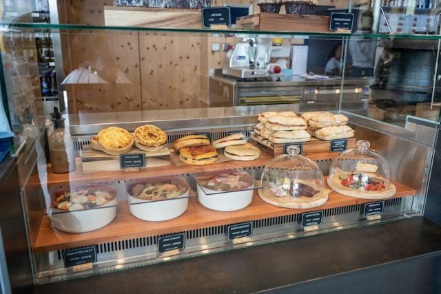 Scatla – pront’ a manger mit einer langen Bedienungstheke. In einer grossen Glasvitrine an der Theke sind verschiedene Speisen und Backwaren ausgestellt. Hinter der Theke befinden sich weitere Auslagen und eine mit hellem Holz verkleidete Wand.