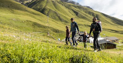 Familienangebote | Corviglia | Sommer Eine vierköpfige Familie gemeinsam am Wandern auf Marguns. Im Hintergrund ist die Bergstation Marguns und die grüne Berglandschaft des Engadins.