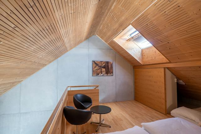 Schlafbereich eines Studio XL der Inn Lodge. Im Bild steht ein schwarzer Nachttisch mit zwei schwarzen Stühlen. Der Raum hat einen Holzboden, eine teilweise holzverkleidete Wand und eine sichtbare Dachschräge.