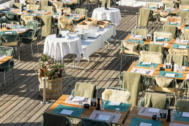 Sonnige Terrasse des White Marmot auf Corviglia mit gedeckten Tischen, Lammfellen auf den Stühlen und Sitzplätzen.