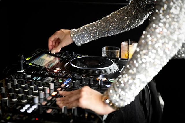 Restaurant White Marmot | Corviglia St. Moritz DJane steht hinter einem DJ-Pult im White Marmot beim Lunch & Dance-Event. Sie trägt ein glitzerndes Oberteil und bedient das Mischpult