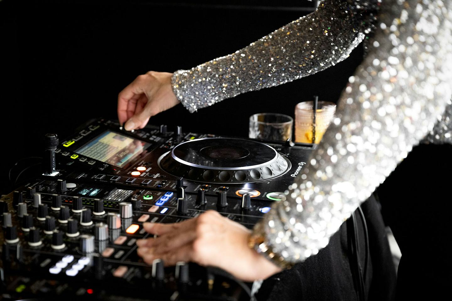 DJane steht hinter einem DJ-Pult im White Marmot beim Lunch & Dance-Event. Sie trägt ein glitzerndes Oberteil und bedient das Mischpult