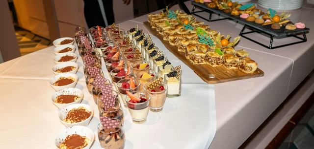 Dessertbuffet im White Marmot mit zahlreichen angerichteten Süssspeisen auf zwei weiss gedeckten Tischen. Im Vordergrund stehen kleine Schalen mit einem mit Kakaopulver bestreuten Dessert sowie Gläser mit verschiedenen Desserts, die unter anderem mit Beeren, Früchten und Schokoladendekorationen garniert sind. Auf den Tischen liegen ausserdem mehrere längliche Stücke eines Gebäcks auf Holzbrettern sowie kleine Törtchen und weitere Süssspeisen. Im Hintergrund sind gestapelte weisse Teller und eine teilweise sichtbare Person zu sehen.