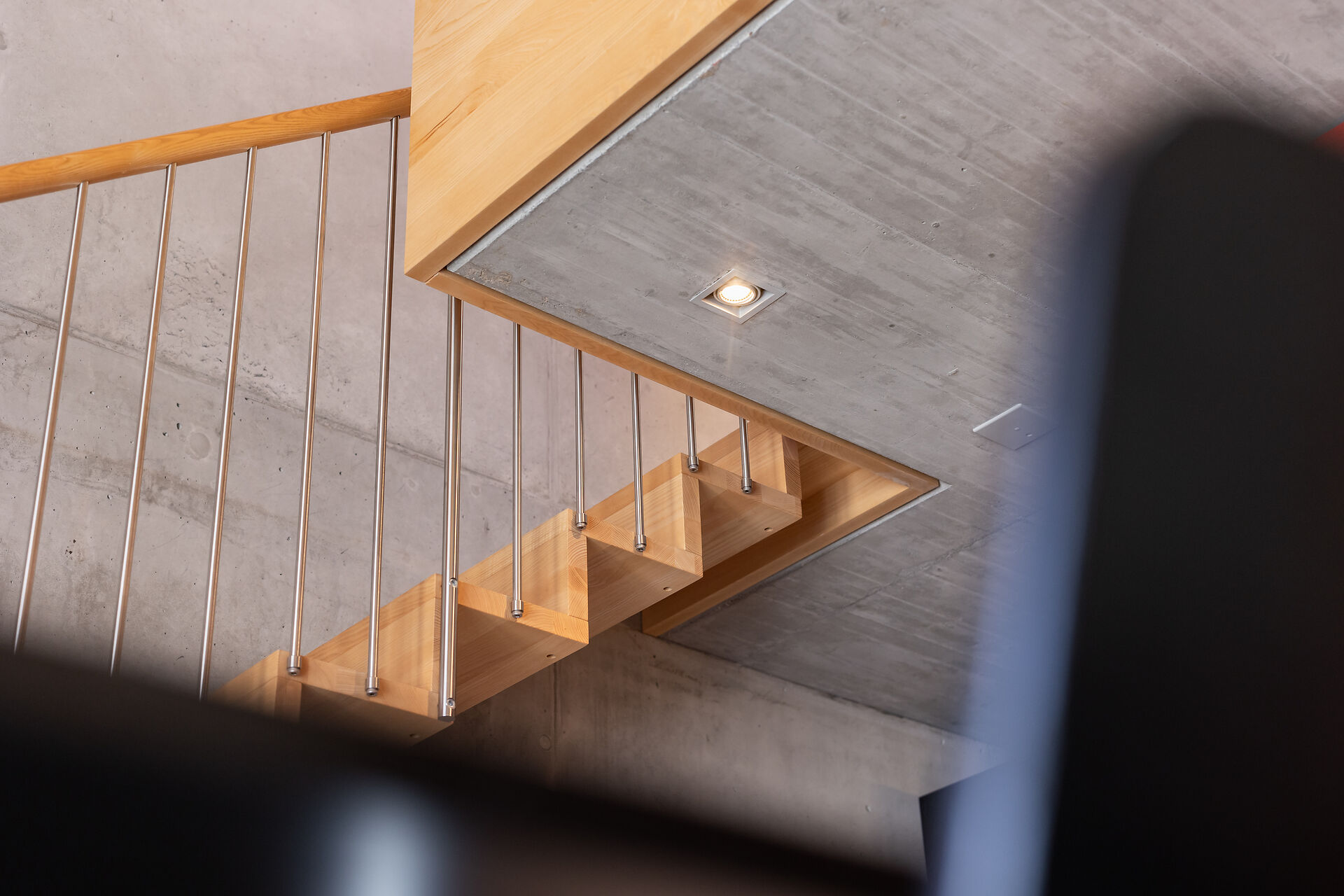 Im Zimmer führt eine offene Holztreppe mit Metallgeländer nach oben.