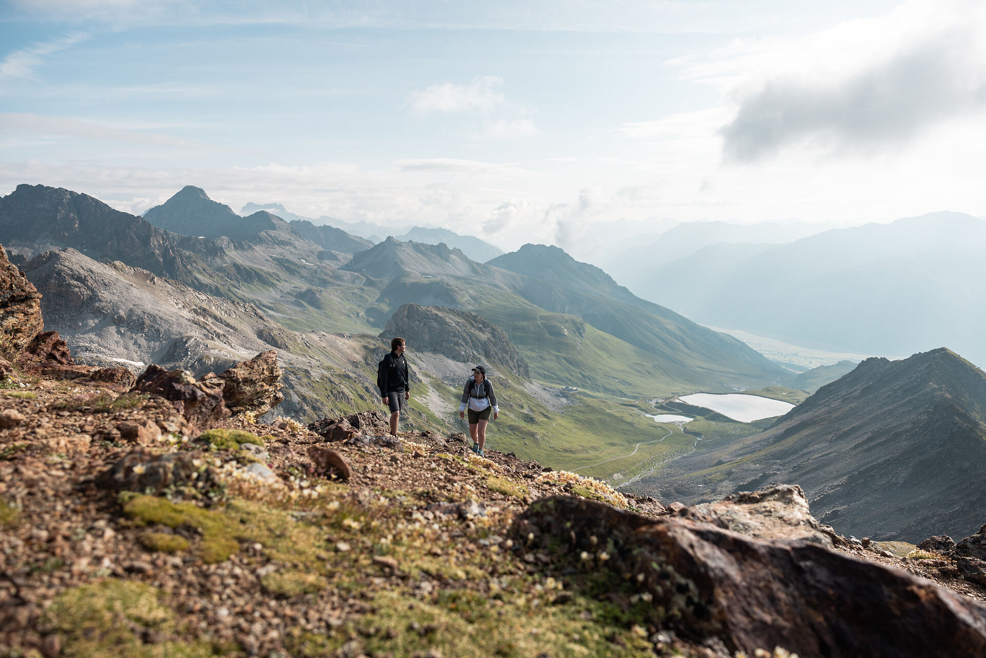 Wandern | Corviglia | Sommer Zwei Wanderer auf Corviglia mit Blick auf den Naturspeichersee und ins Engadiner Tal.