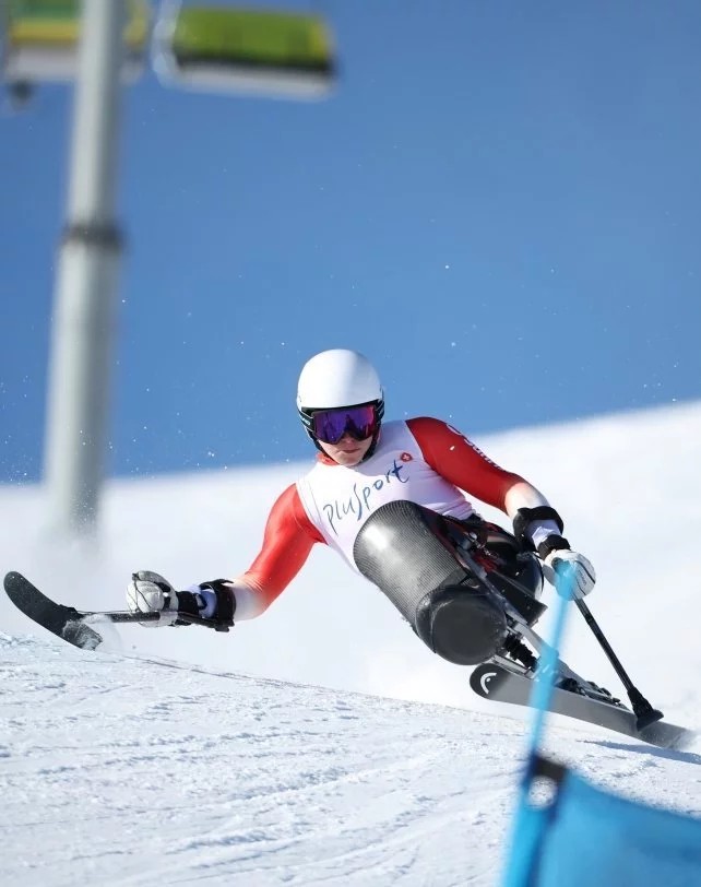 Skifahrer mit Monoskibob in roter Skibekleidung und weissem Helm fährt auf einer verschneiten Skipiste auf der Corviglia durch ein blau markiertes Tor.