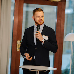 Jack in a suit and tie holding a microphone and giving a presentation.