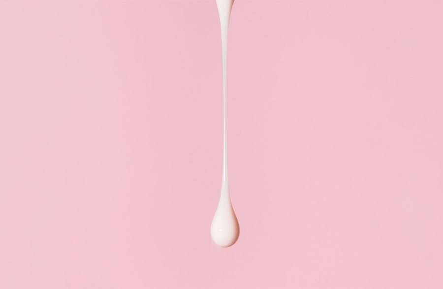 Drop of thick white fluid on a light pink background.