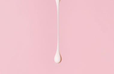 Drop of thick white fluid on a light pink background.