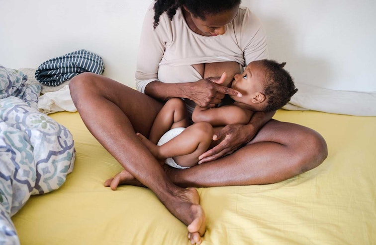 Woman sat on messy bed breastfeeding a baby