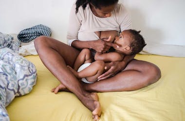 Woman sat on messy bed breastfeeding a baby
