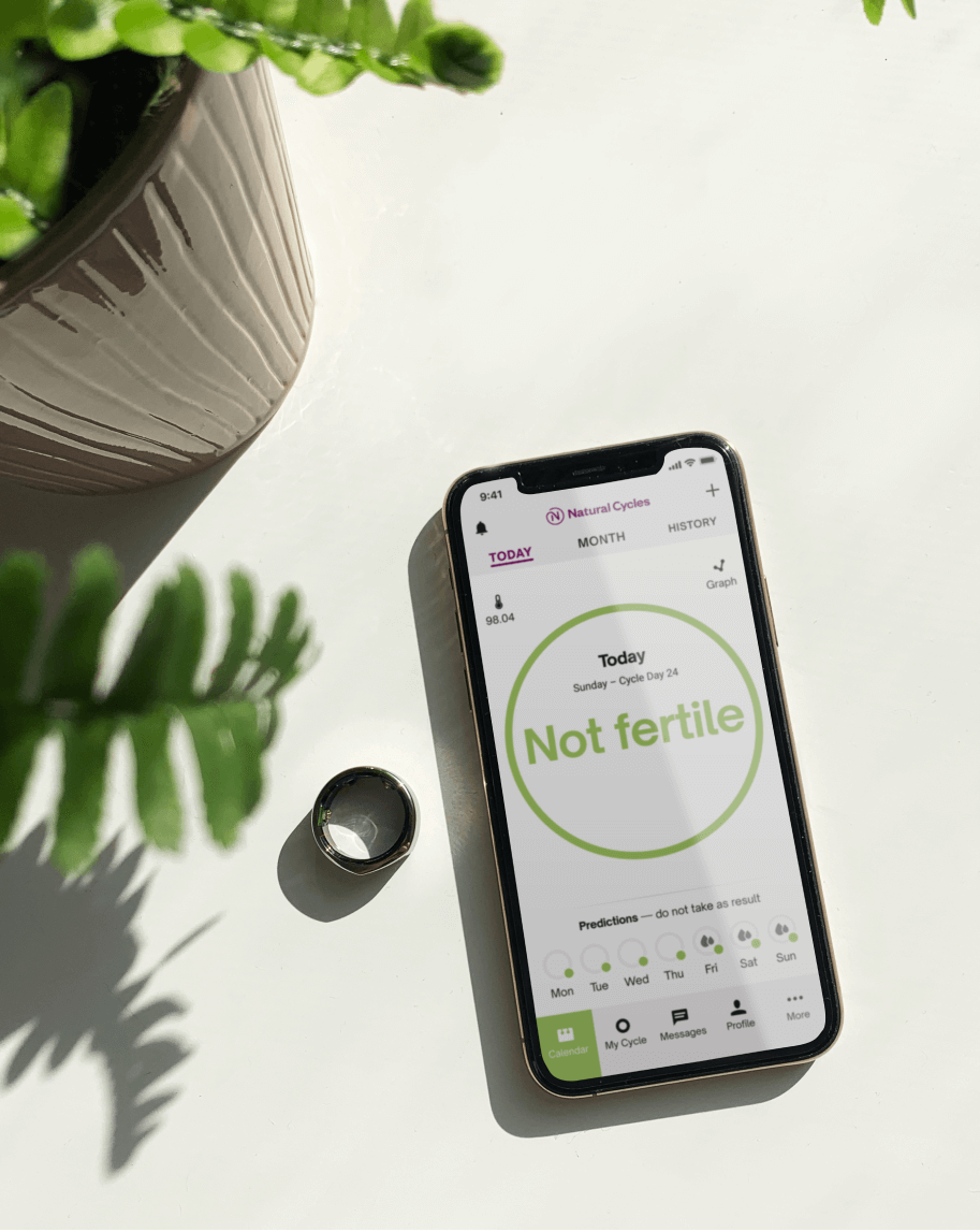 An iPhone displaying the Natural Cycles app, next to an Oura ring and a pot plant