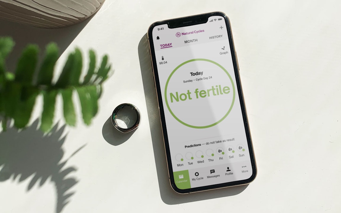 An iPhone displaying the Natural Cycles app, next to an Oura ring and a pot plant