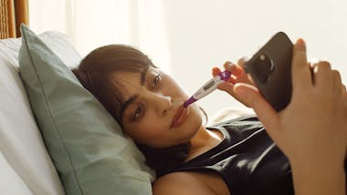 Woman in bed measuring her temperature and looking at a phone