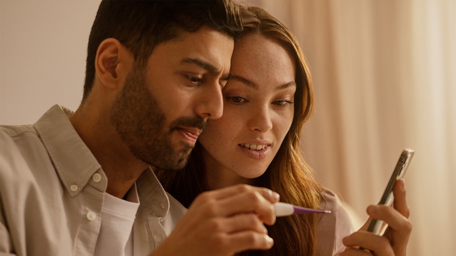 Man and woman holding thermometer and looking at phone together